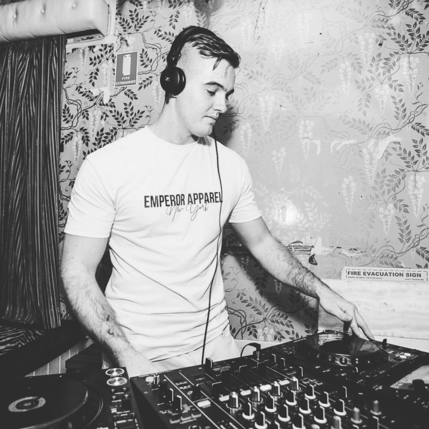 Michael McMahon stands behind DJ decks in black and white
